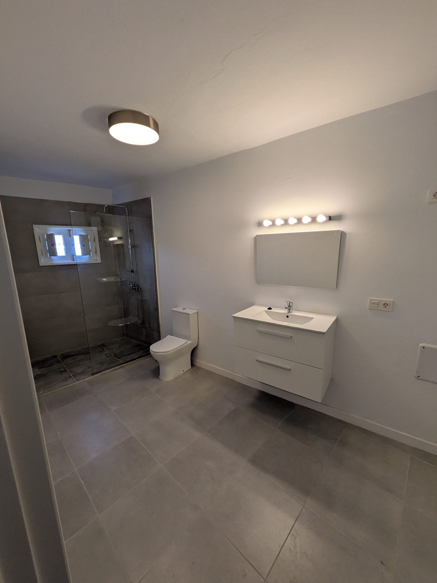 Baño reformado por Terraform en Tinajo, Lanzarote, con ducha de obra, mampara de cristal y mueble de lavabo suspendido