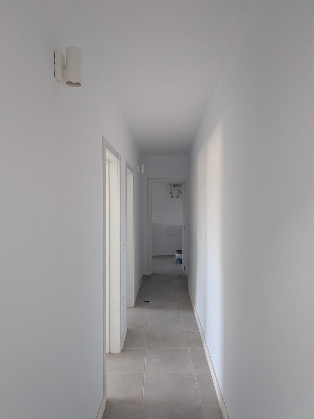 El mismo pasillo terminado, con paredes lisas pintadas, pavimento nuevo, puertas montadas y luz de pared